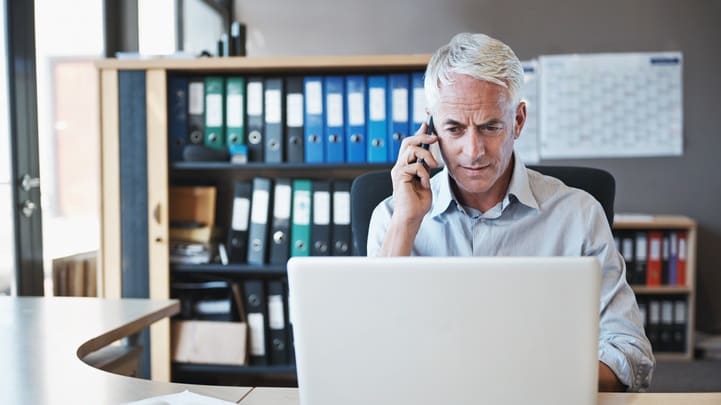 A man sitting at a desk with a laptop and a cell phone.