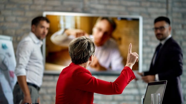 A group of people in a conference room pointing at a tv screen.