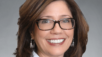 A woman wearing glasses and a suit smiles.