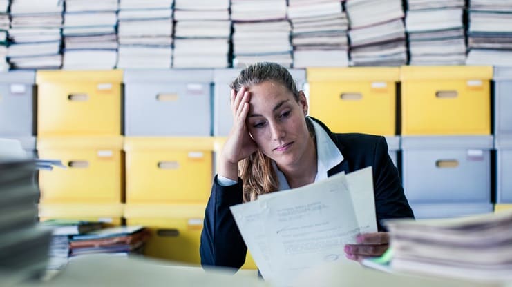 A woman is sitting in front of a pile of papers.