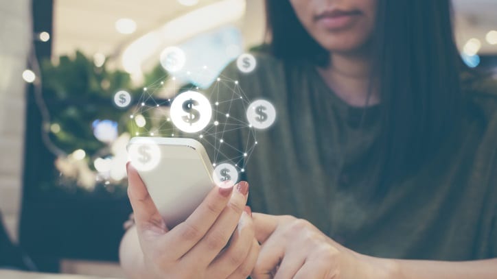 A woman using a smartphone with money icons on it.