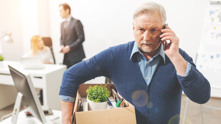 Senior man talking on the phone while carrying a box in the office.