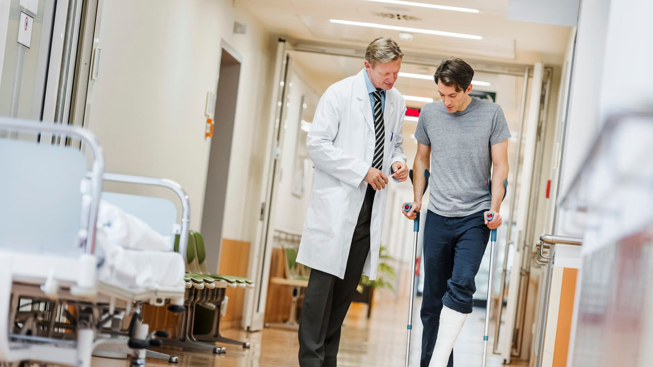 A man with a broken leg is walking down a hospital corridor.
