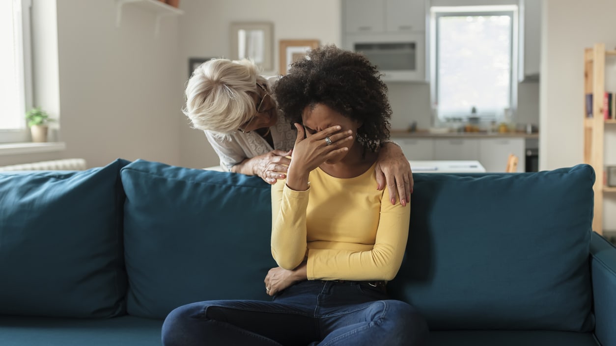 A woman is sitting on a couch with her hands on her face.