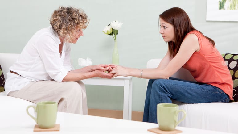 Two women sitting on a couch talking to each other.