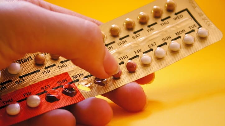 A hand holding a pack of contraceptives on a yellow background.