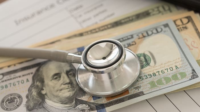 A doctor's stethoscope sits on top of a stack of bills.