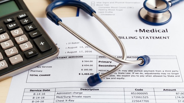 A stethoscope and a calculator sit on top of a medical bill.