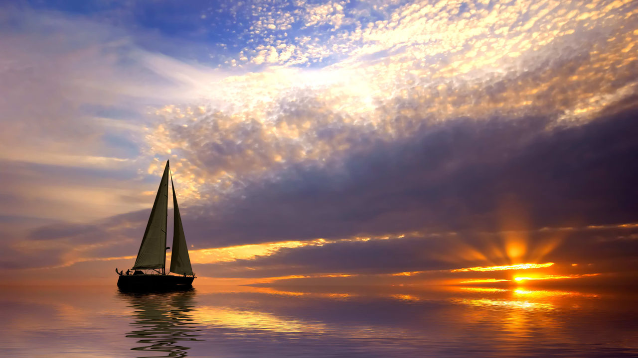 A sailboat sails across the water at sunset.