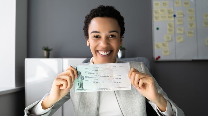 A woman holding up a check in an office.