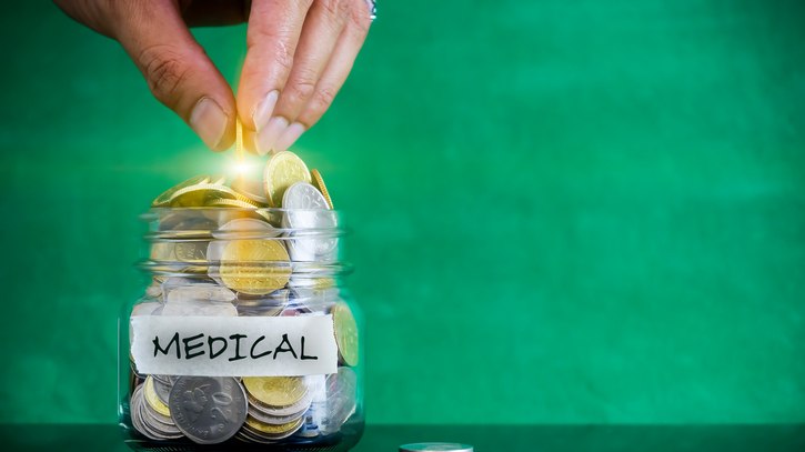 A hand putting coins into a jar with the word medical on it.