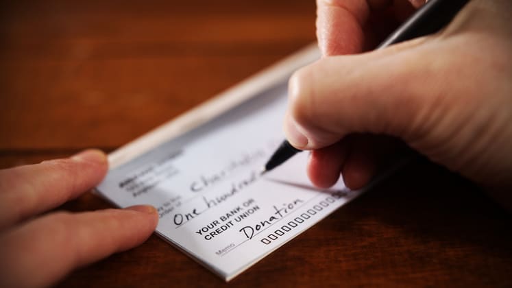 A person signing a check on a wooden table.