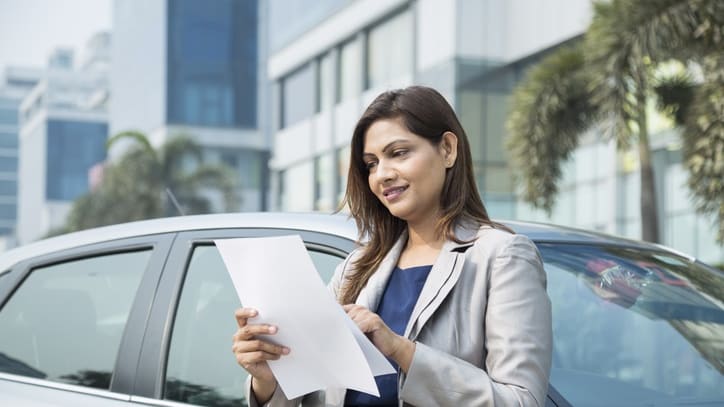 A business woman holding a piece of paper in front of her car.