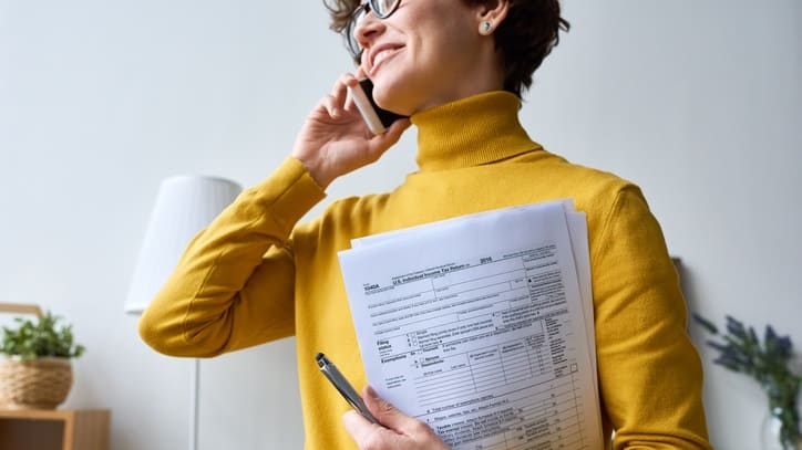A woman holding papers while talking on the phone.