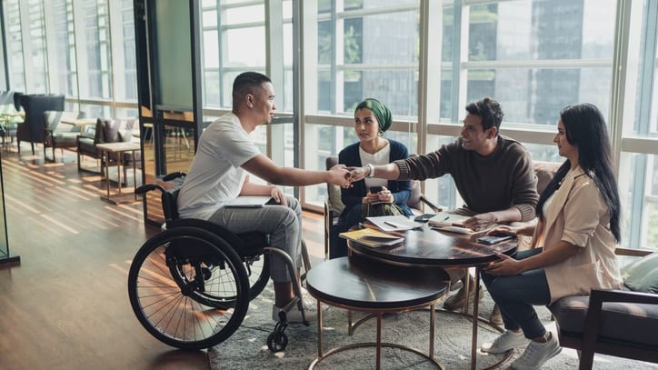 A group of people shaking hands at a table with a person in a wheelchair.