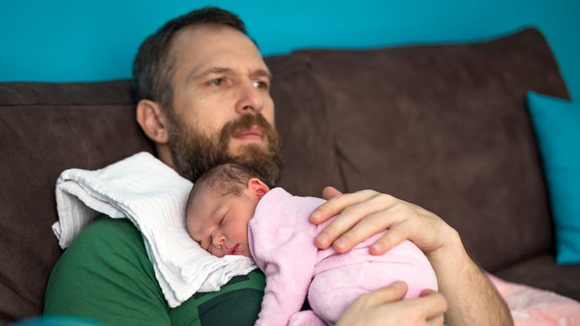 A man with a beard holding a baby on a couch.