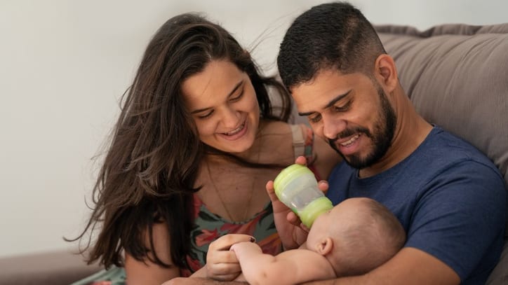 A man and woman feeding a baby with a bottle.