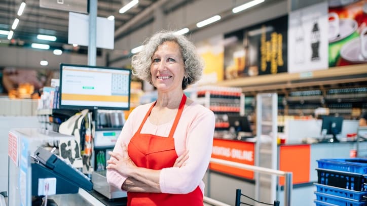 A woman in a red apron standing in a grocery store.