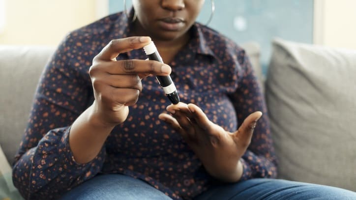 A woman sitting on a couch holding a blood glucose meter.