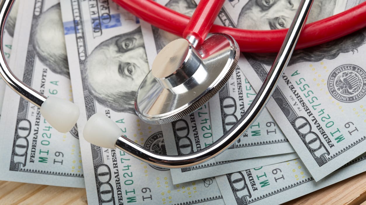 A stethoscope sits on top of a pile of money.
