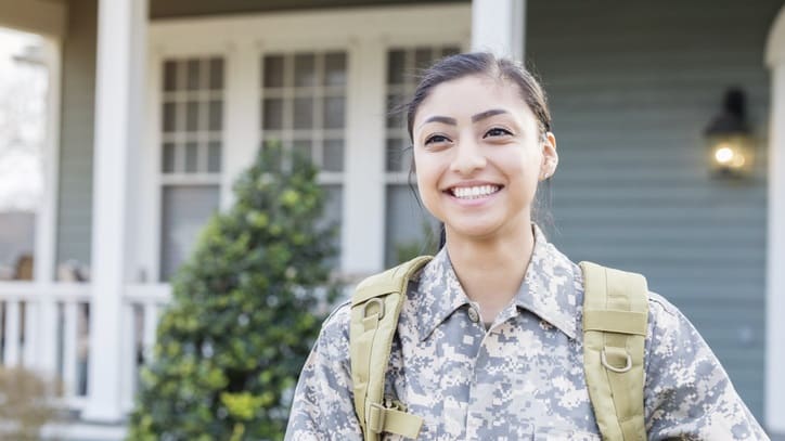 A woman in military uniform smiling in front of a house.