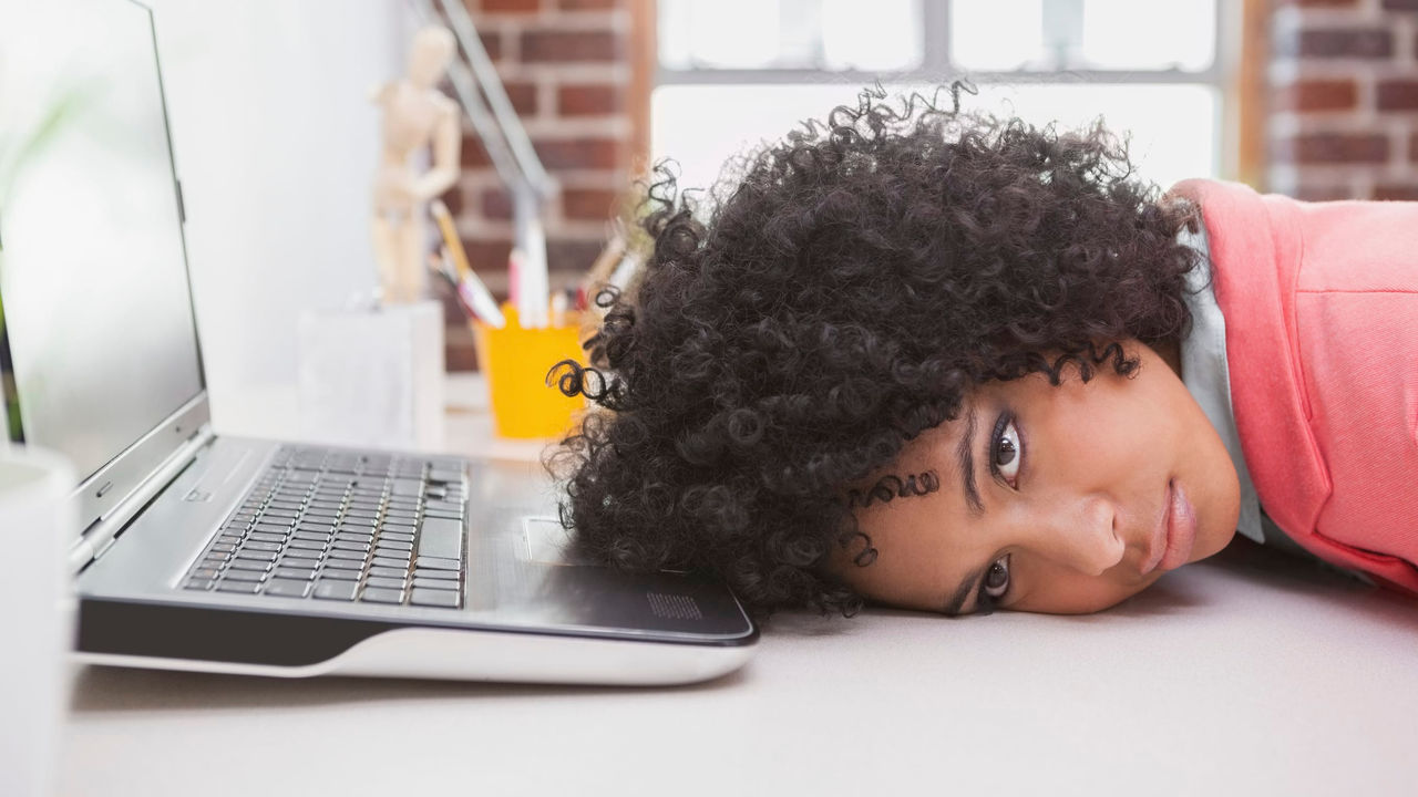 A woman laying on her back on a desk with a laptop.