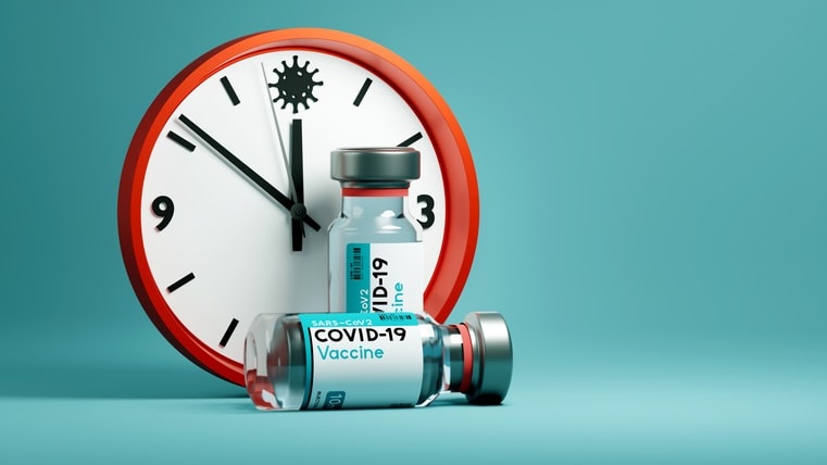 A clock next to a bottle of coronavirus vaccine.