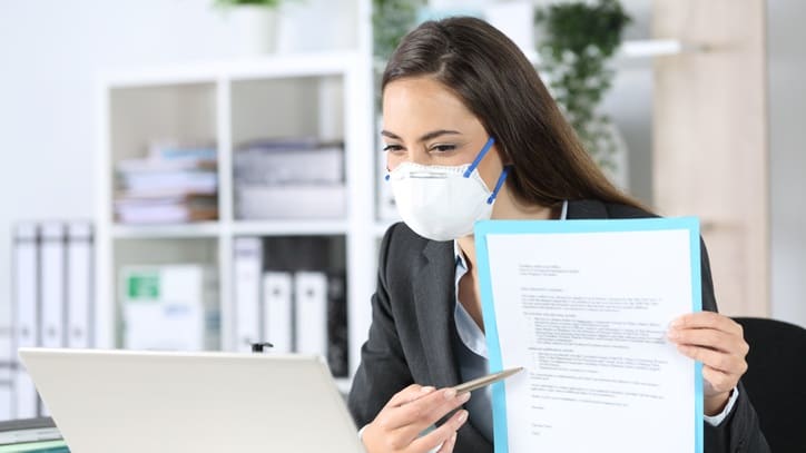 A woman wearing a face mask while working on a laptop.