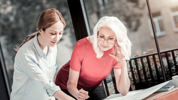 Two women looking at blueprints at a table.