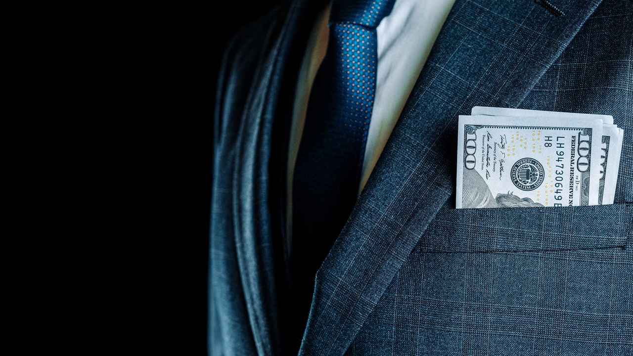 A man in a suit with a dollar bill in his pocket.