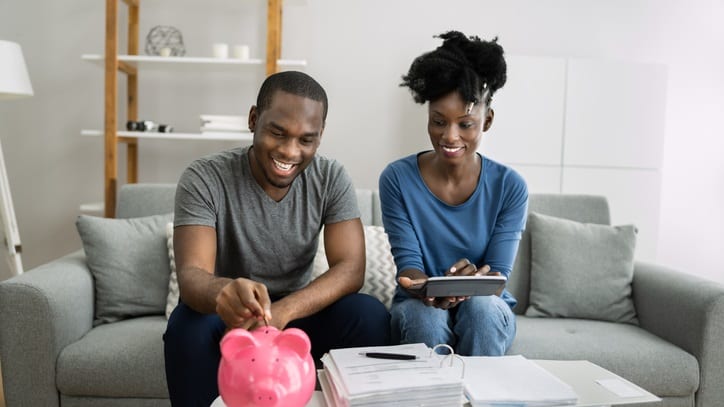 A couple sitting on a couch with a pink piggy bank.