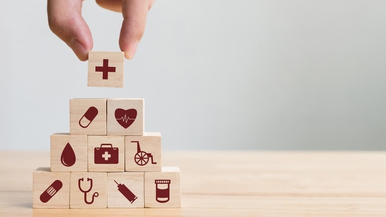 A hand is holding wooden blocks with medical icons on them.