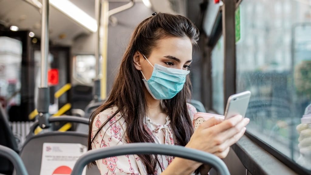 A woman wearing a surgical mask on a bus.