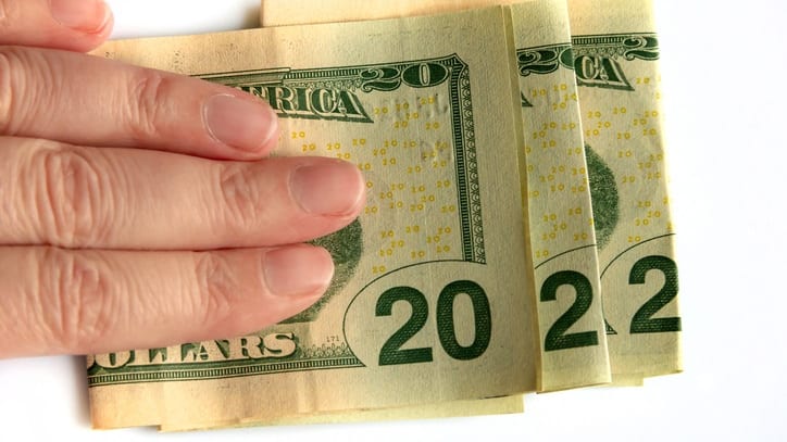 A person's hand holding a stack of twenty dollar bills.