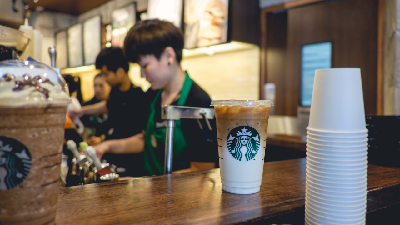 A starbucks employee is preparing a cup of iced coffee.