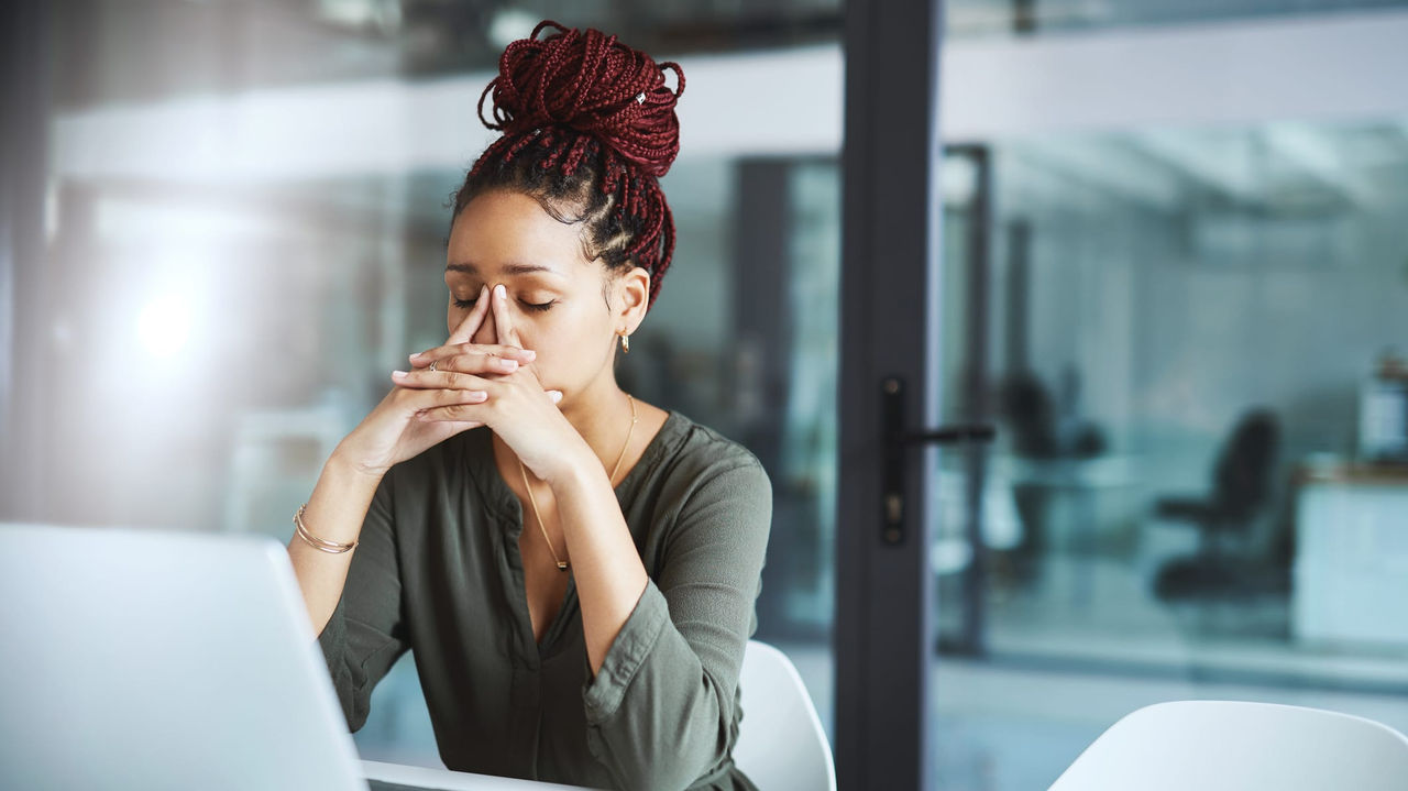 A woman is sitting at a desk with a laptop in front of her face.