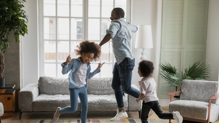 A dad and his children playing, dancing, and jumping in a living room.