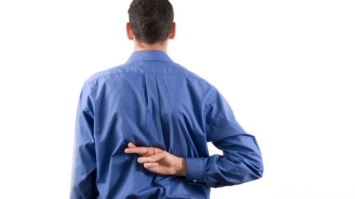 A man in a blue shirt is holding his back against a white background.