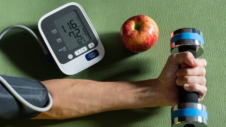 A man's hand holding a blood pressure monitor and an apple.