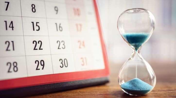 An hourglass with blue sand in front of a calendar.