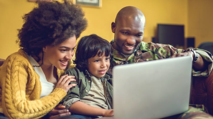 A family is sitting on a couch looking at a laptop.