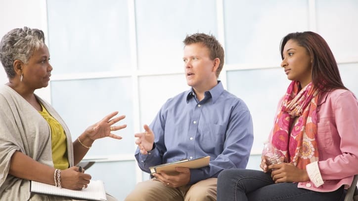 Three people sitting in chairs talking to each other.