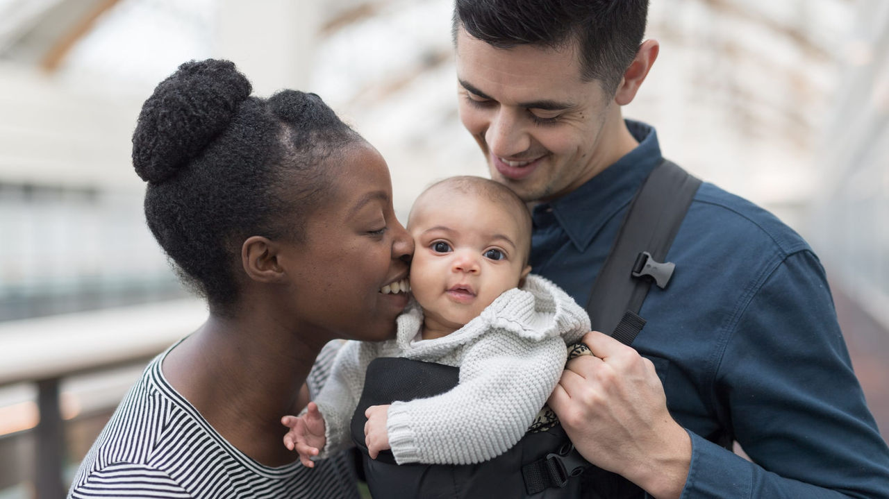 A man and woman holding a baby in a baby carrier.