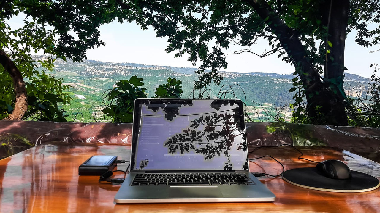 A laptop sits on a wooden table with a view of the mountains.