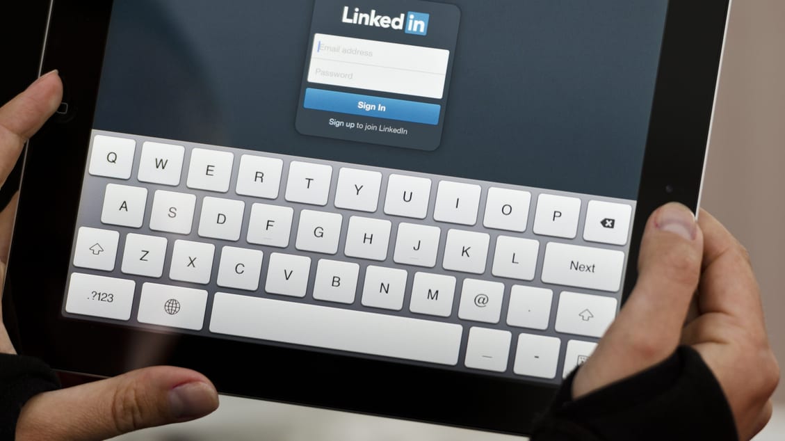 A person holding an ipad with the linkedin logo on it.