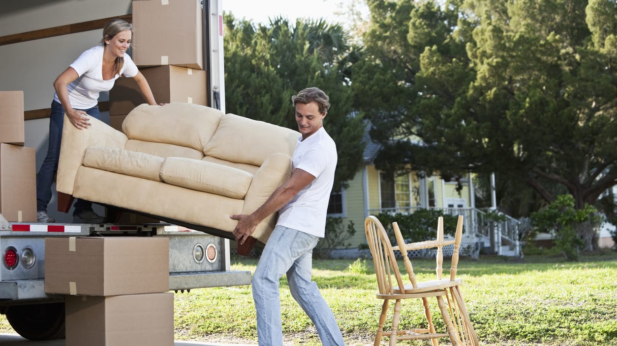 A man and woman moving a couch into a moving truck.