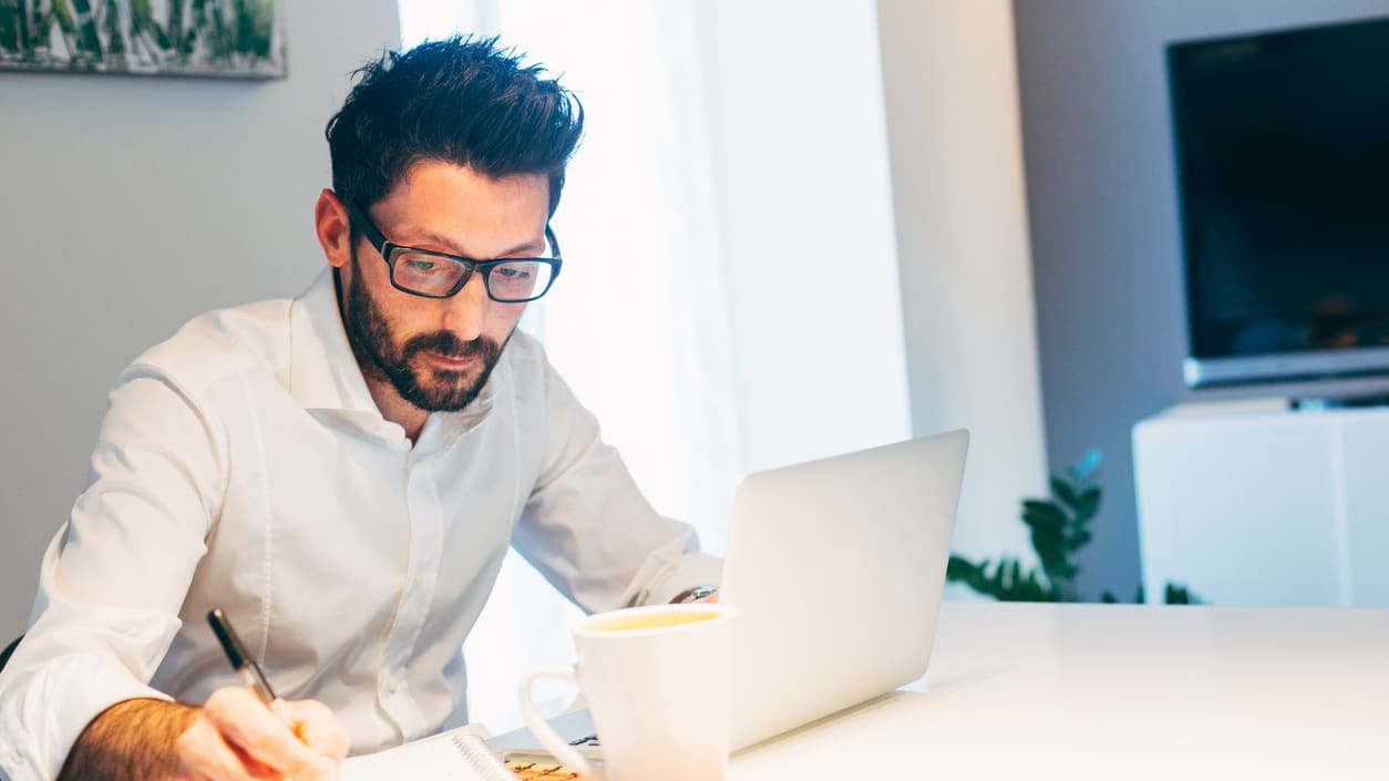 A man working on a laptop in front of a cup of coffee.