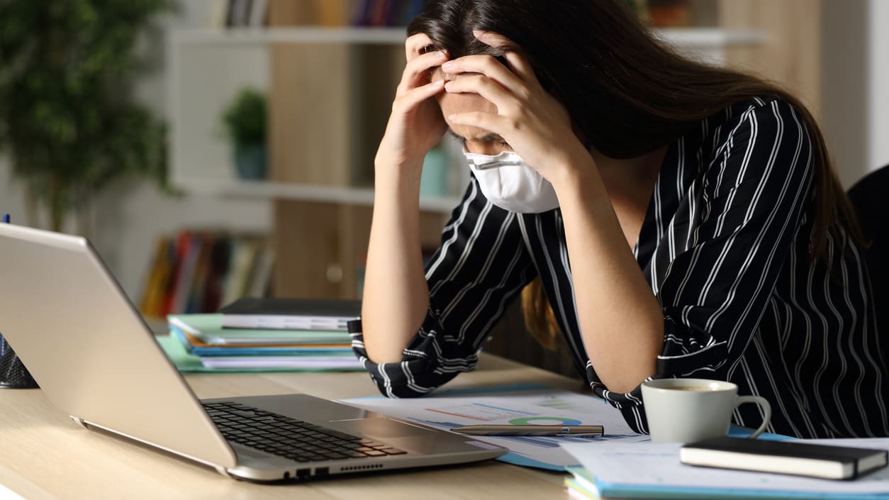 A woman wearing a face mask is sitting at a desk with a laptop.