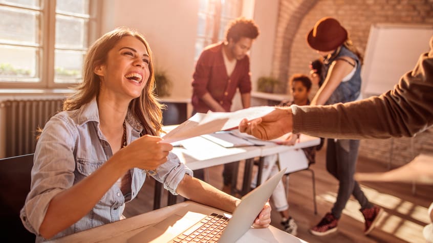 A woman handing a woman a piece of paper in an office.