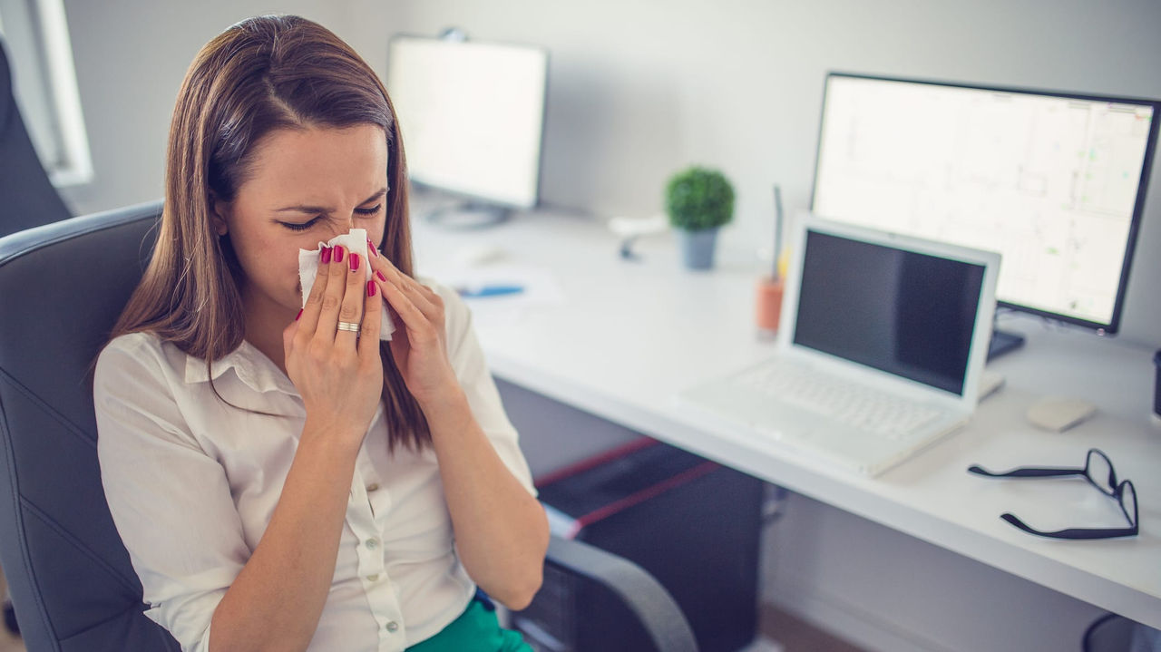 A woman sneezing in an office chair.